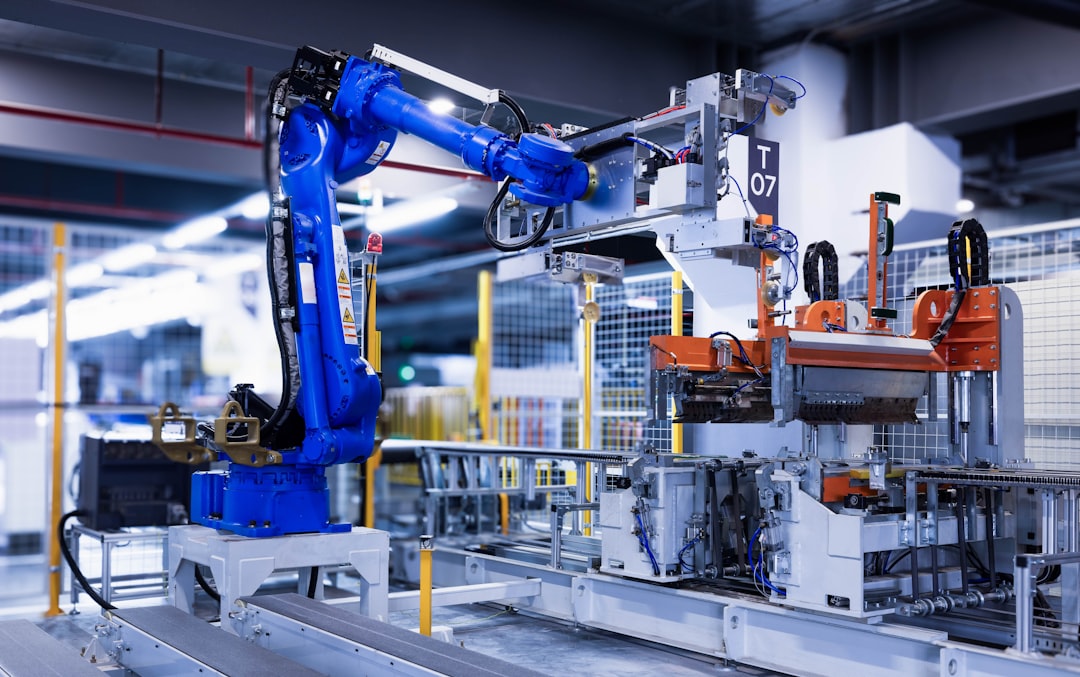 Blue industrial robot arm operating at a production line with conveyors and orange clamps in a safe fenced area