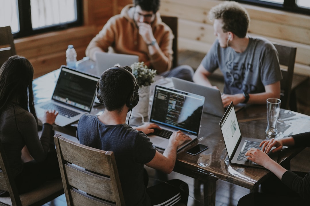 Group of people coding on laptops around a wooden table in a casual workspace.