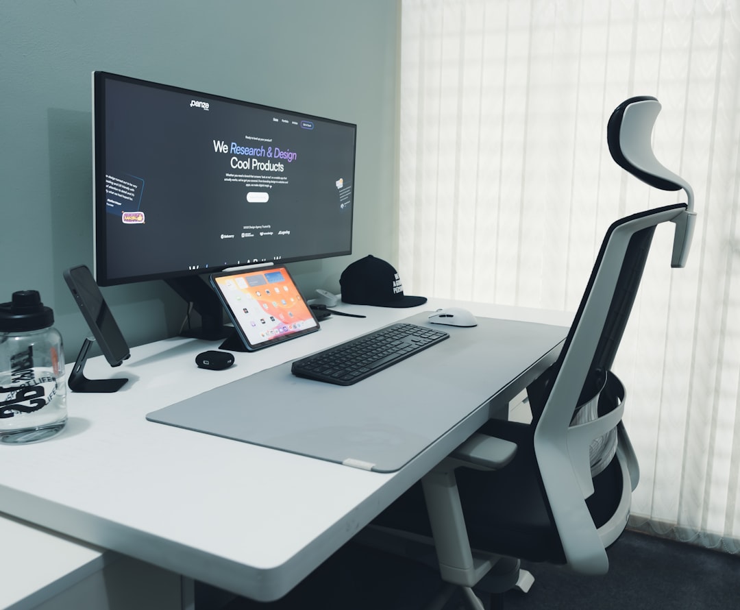 Modern desk setup with a large monitor, tablet, keyboard, and ergonomic chair in a bright office space.