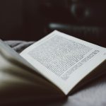Open paperback book resting on a soft blanket, pages fanned as it lies on a bed.