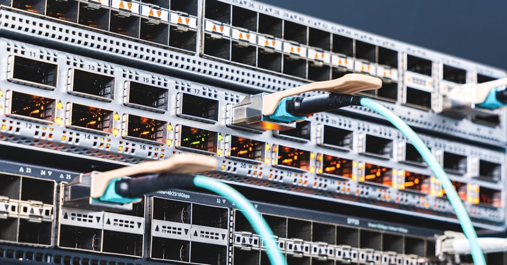 Rack of network switches with orange activity LEDs and teal Ethernet cables connected, in a data center rack