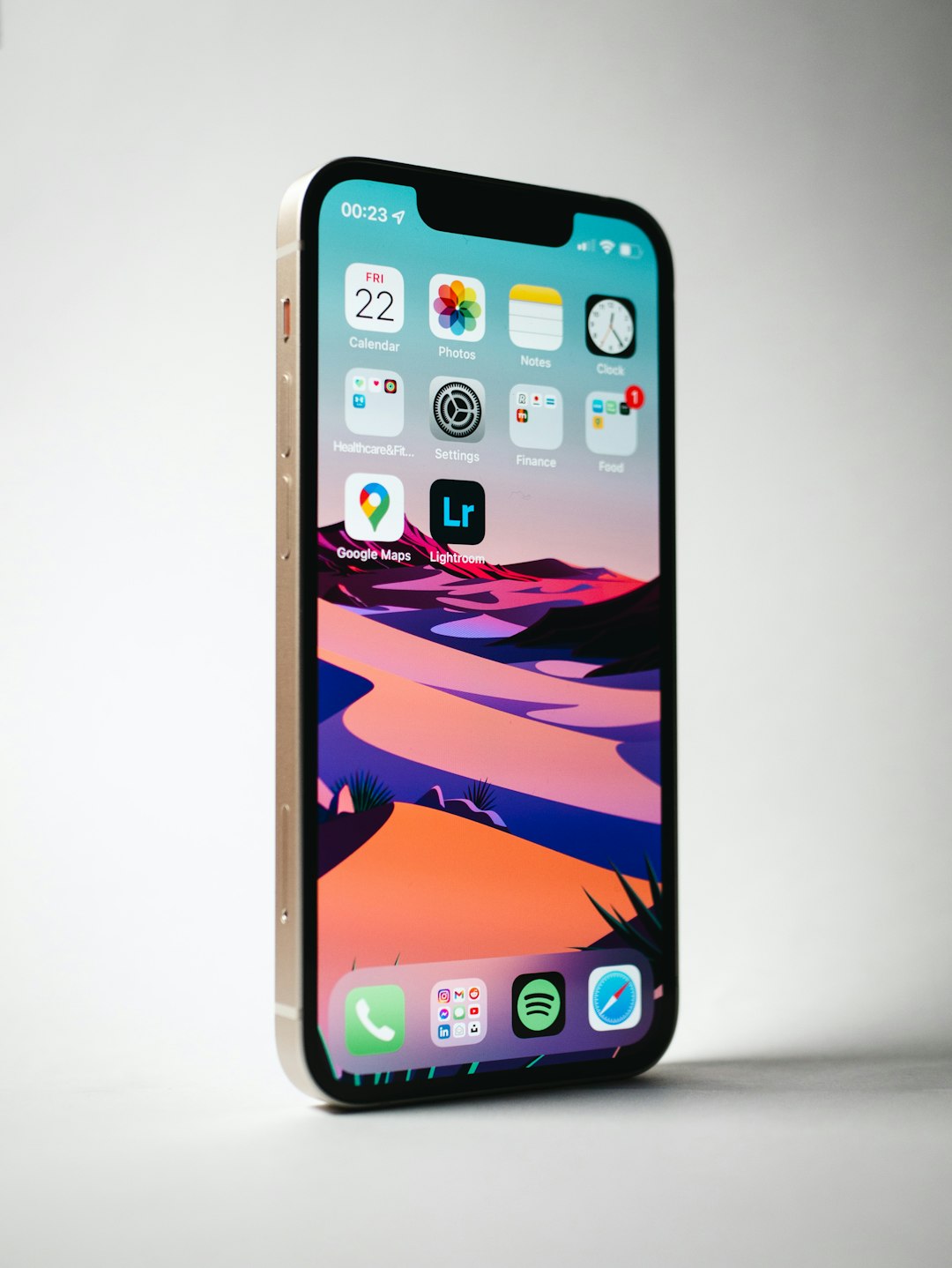 Gold iPhone standing upright showing its home screen with colorful app icons and a landscape wallpaper.