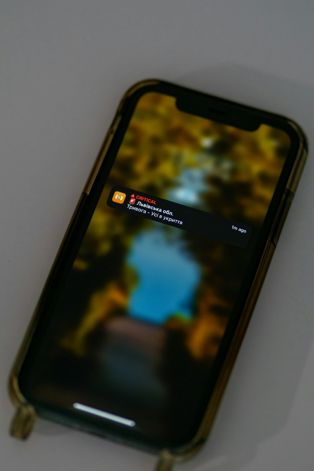 Smartphone screen showing a critical alert notification in Ukrainian about an air raid and to shelter, overlaying a blurred outdoor background.