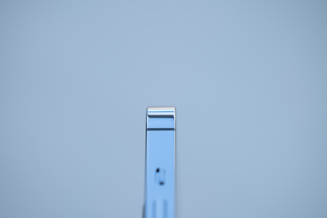 Close-up of a vertical chrome metal strip with a rounded top against a pale blue background, minimal and abstract.
