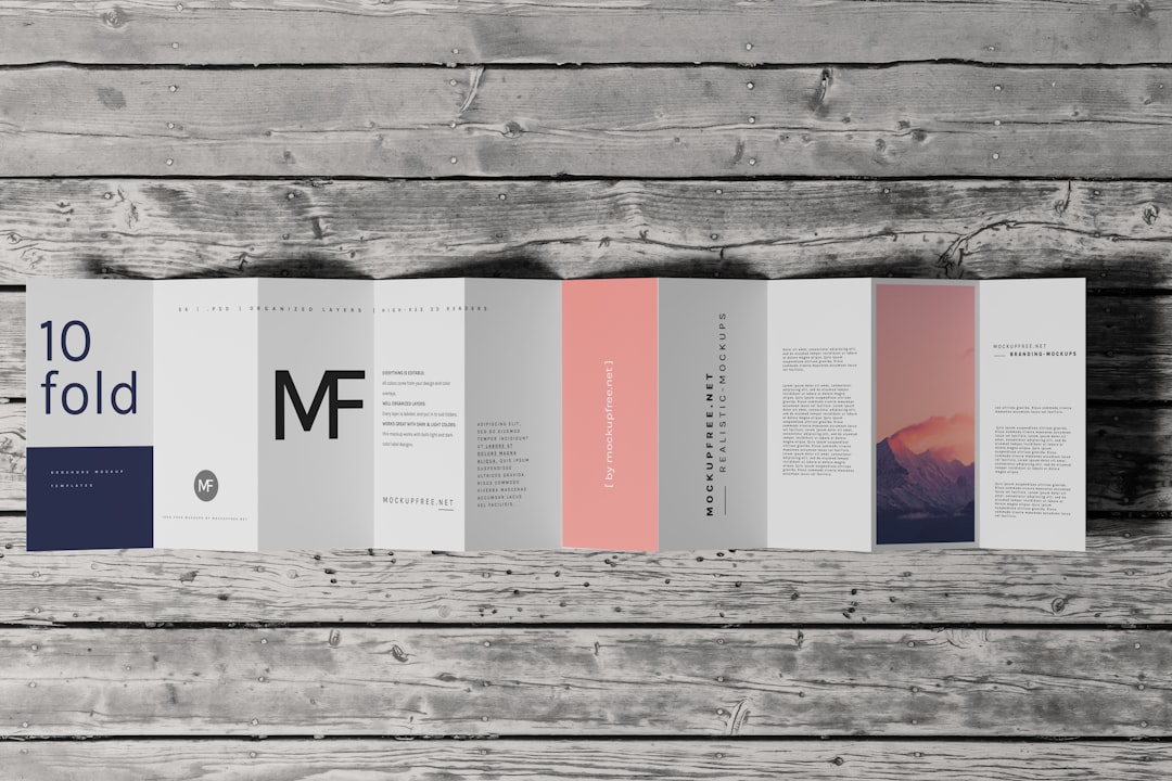 A multi-panel brochure folded open on a rustic wooden table, with '10 fold' text on the left and pastel gray/pink panels.