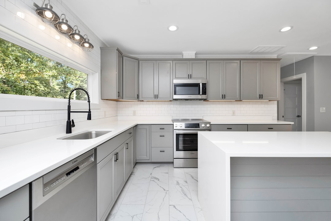 Bright modern kitchen with gray cabinetry, white countertops, and stainless steel appliances around a large island.