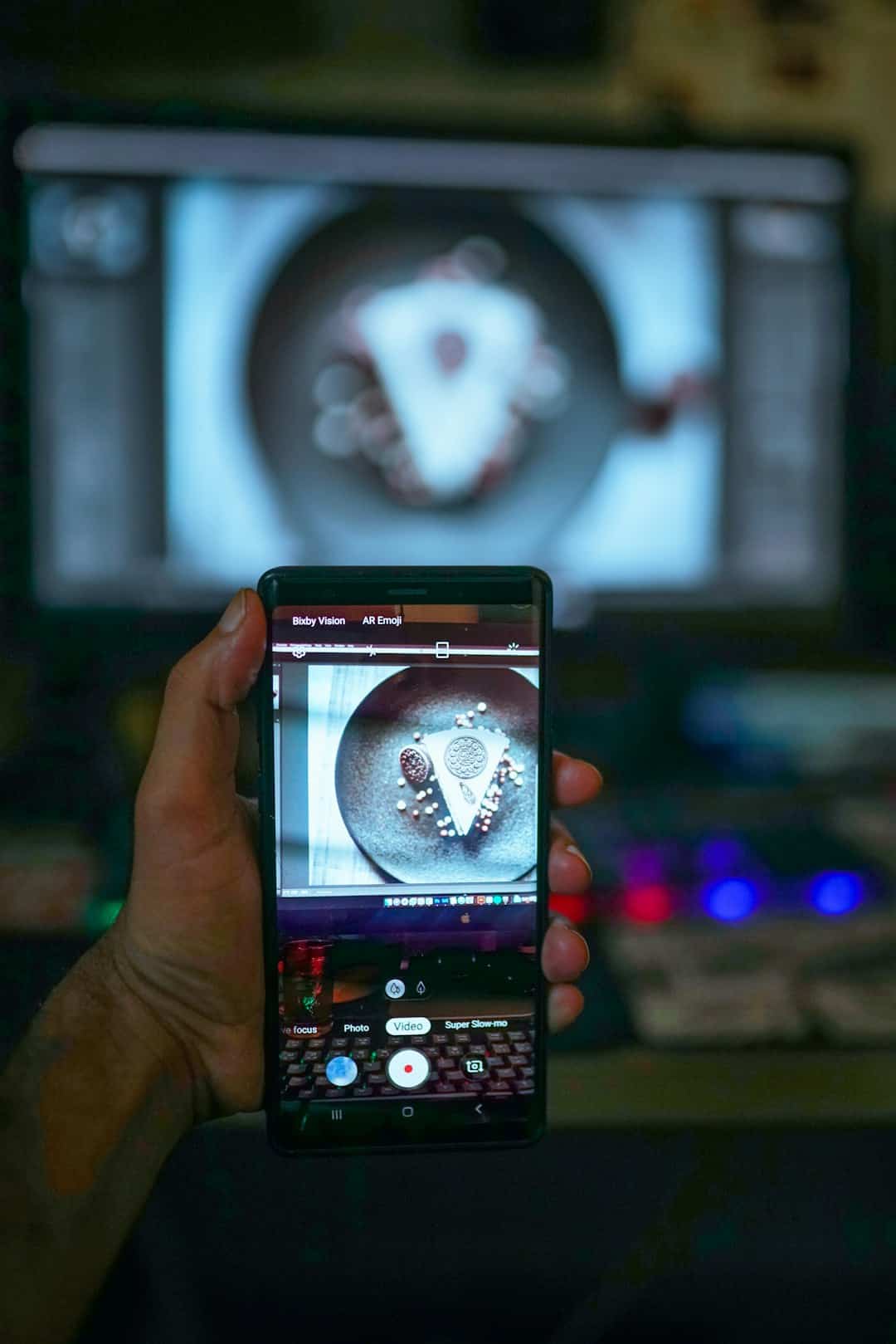 Close-up of a hand holding a phone recording a plate of decorative triangular cookies; the phone screen shows the same plate in focus nearby.