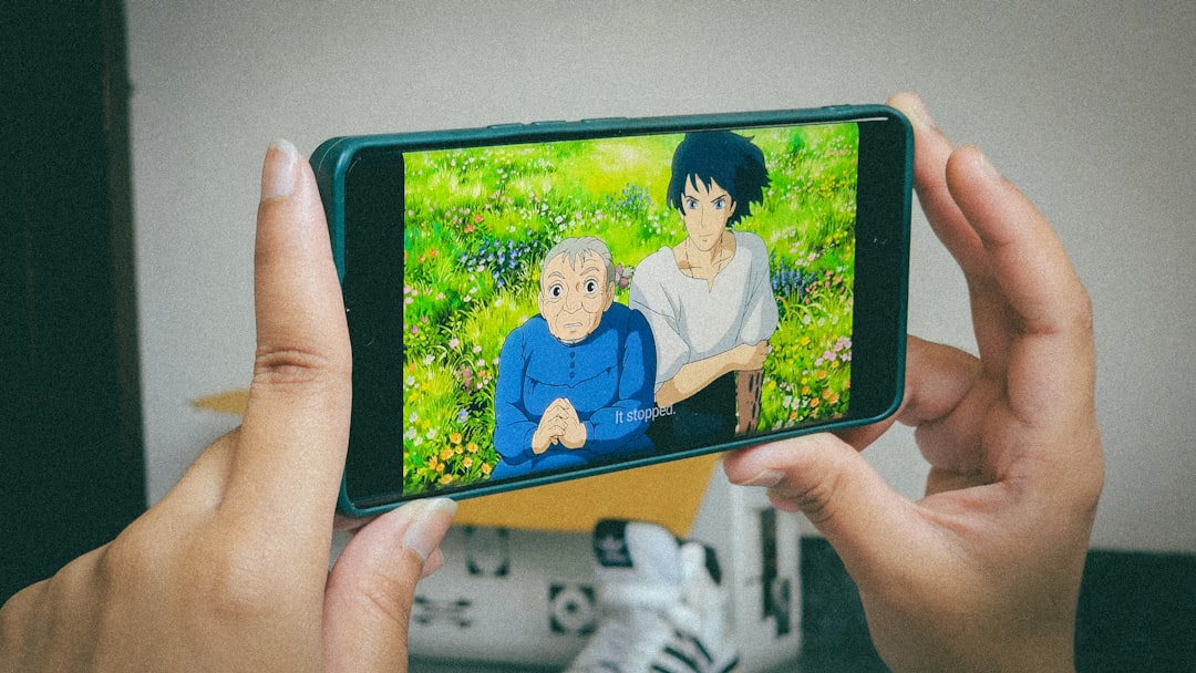 Animated scene on a smartphone screen: an elderly woman and a young man in a bright, flower-filled meadow, held by two hands.
