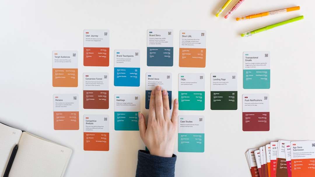 Person's hand arranges color-coded strategy cards on a white desk, planning a branding or marketing project.