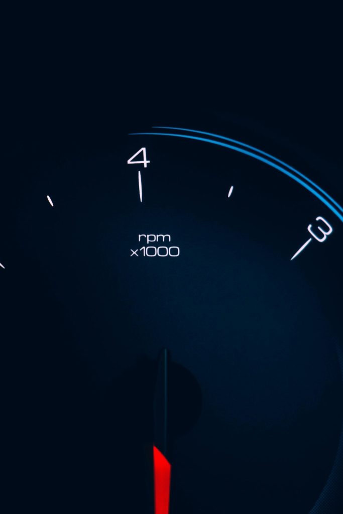 Close-up of a tachometer gauge on a dark dashboard showing ~4,000 RPM with a red needle.