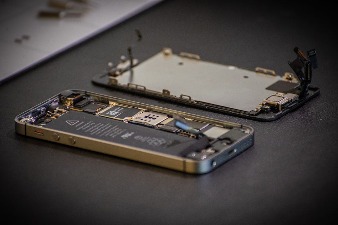 Disassembled smartphone laid open on a dark surface, exposing the battery, circuit board, and back cover pieces laid nearby.