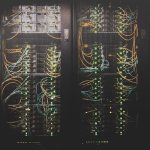 Server racks in a data center with tangled orange and blue network cables and blinking green LEDs.