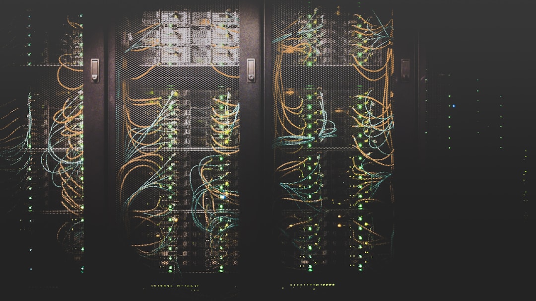 Rows of dark server racks with green and orange cables connected to blinking LEDs in a dim data center.
