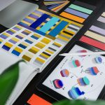 Designer’s desk featuring color swatches and a swatch book, tablet displaying color swatches, and a white stylus for digital color work.