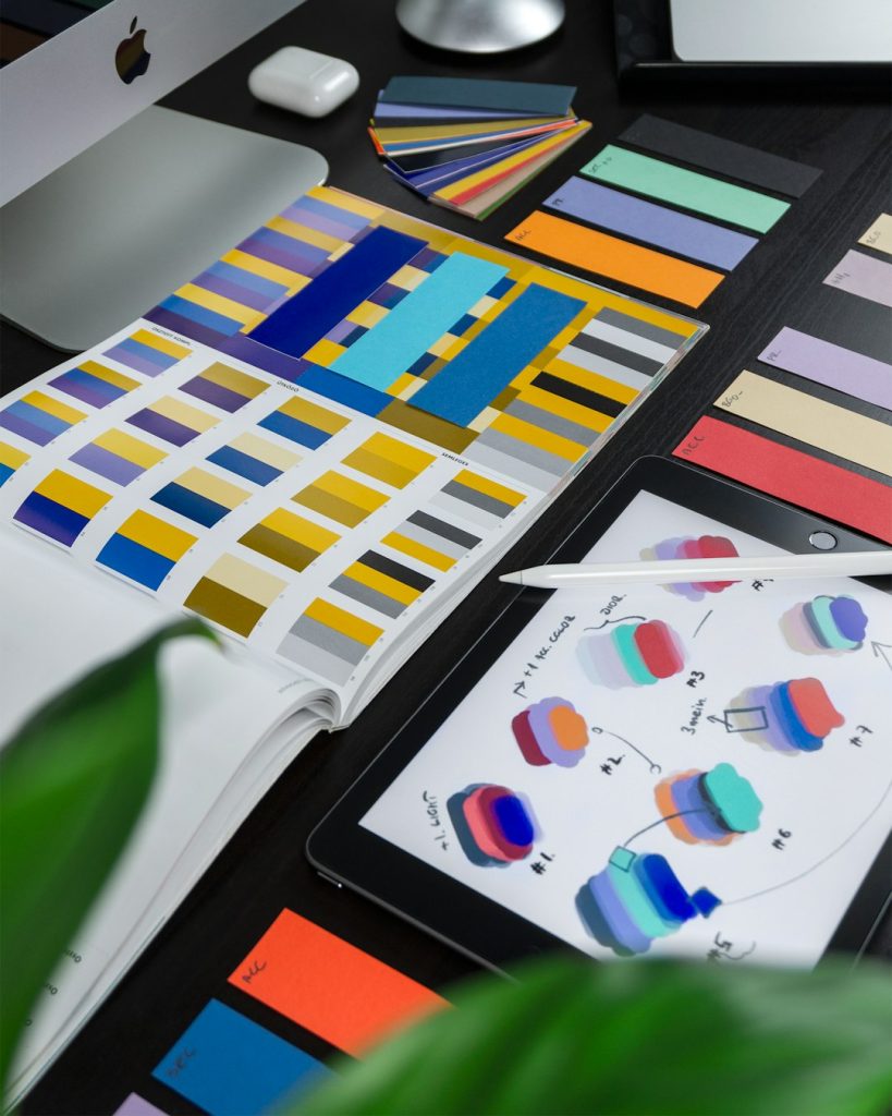 Designer’s desk featuring color swatches and a swatch book, tablet displaying color swatches, and a white stylus for digital color work.