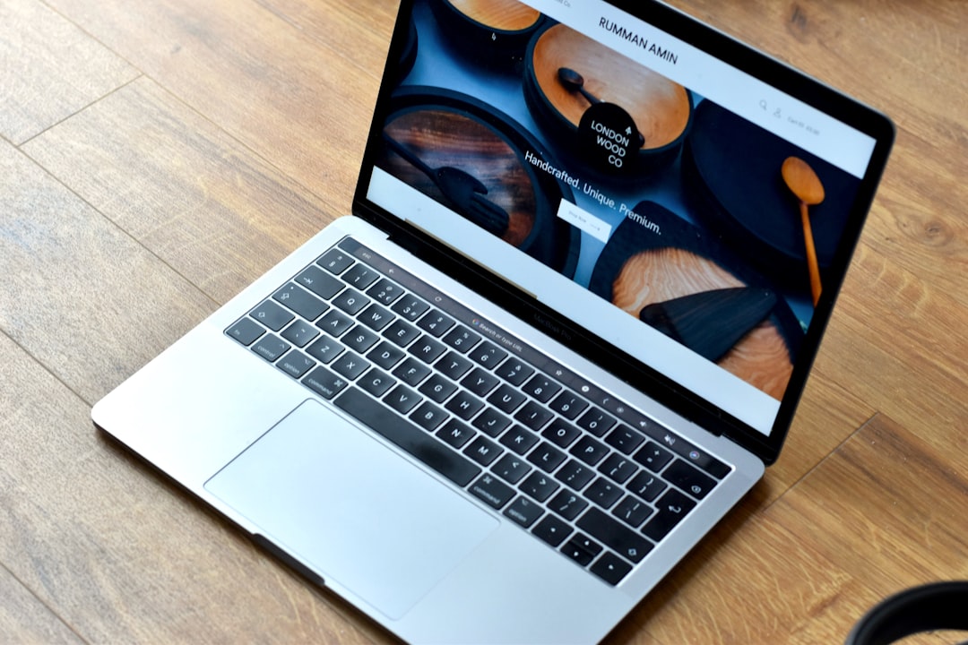 Silver laptop on a wooden floor displaying a cookware website with images of wooden bowls and utensils on the screen.