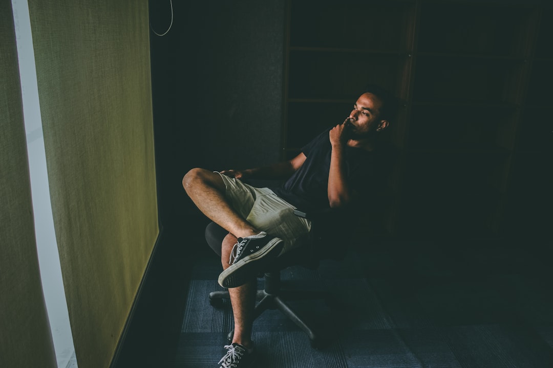 Man seated in a swivel chair in a dark room, chin resting on his hand, deep in thought.