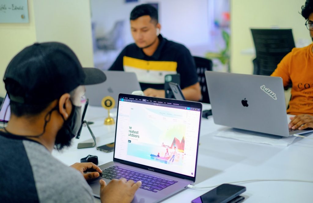 Team of three people working on laptops around a table in a modern coworking space.