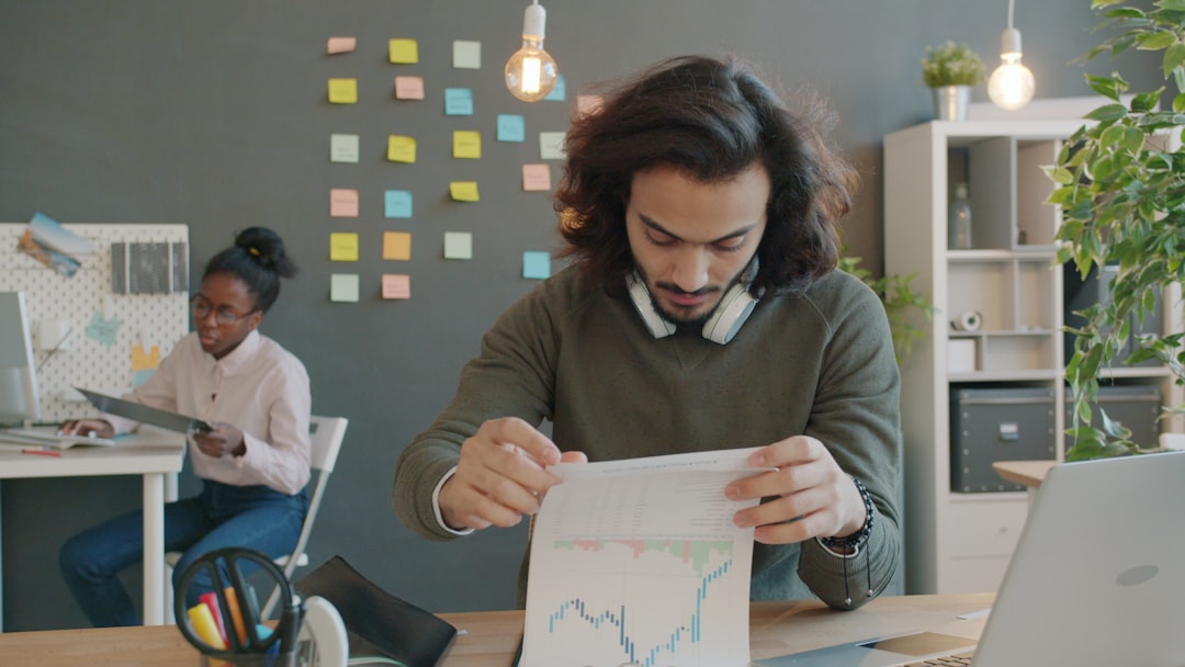 Man with headphones reviews a printed chart at a desk in a modern office.