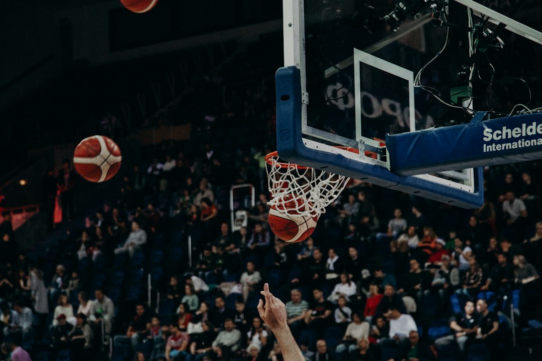 Basketball hoop with ball falling through net as a player raises a finger amid a crowded arena.