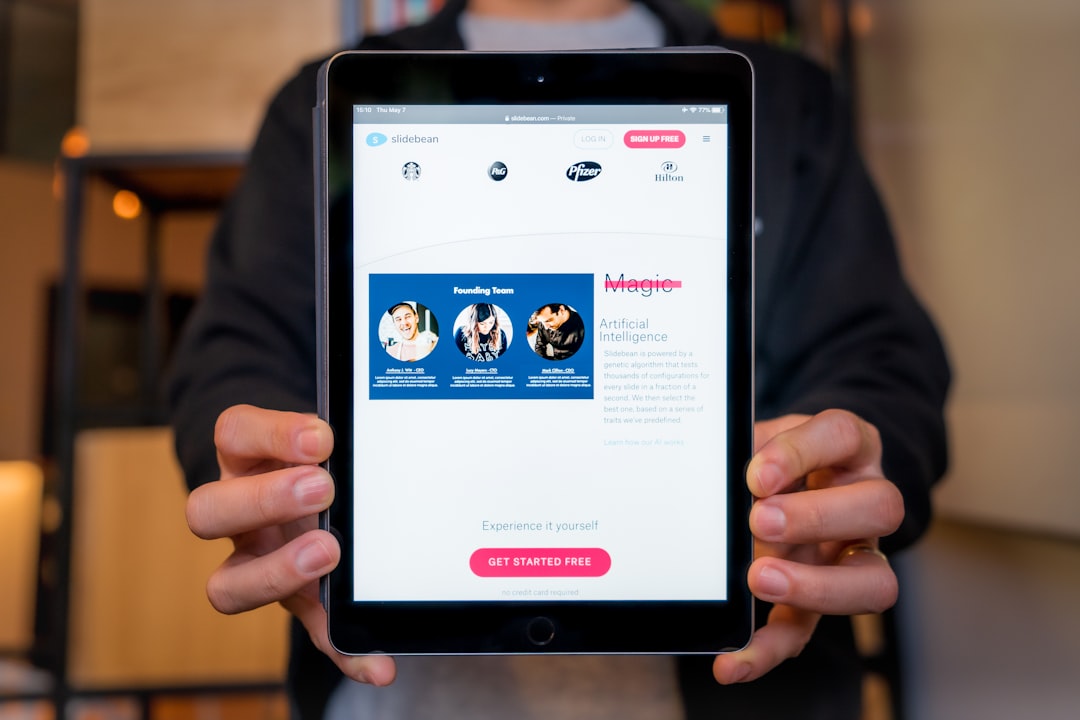 Person holds a tablet displaying a Slidebean landing page with a blue founding team image and a pink 'Get Started Free' button on screen.
