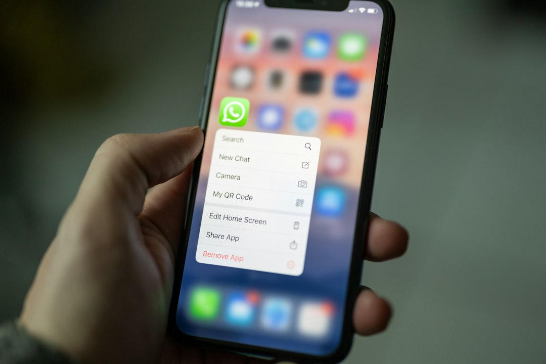 Hand holding an iPhone with WhatsApp options menu open: Search, New Chat, Camera, My QR Code, Share App, Remove App (blurred home screen)