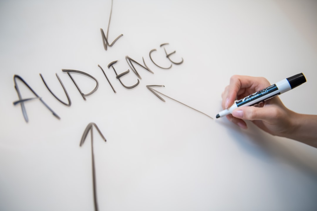 Hand holding a marker writes the word AUDIENCE on a whiteboard with an arrow pointing to it.