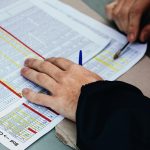 Close-up of hands reviewing a printed schedule or timetable with colored highlights on a desk surface.