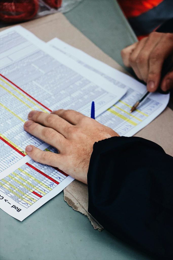 Close-up of hands reviewing a printed schedule or timetable with colored highlights on a desk surface.