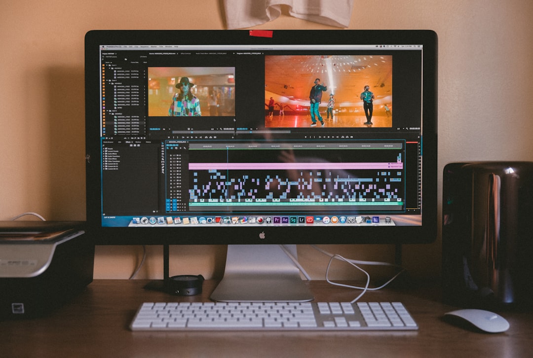 Desktop monitor displaying video editing software with a timeline and two preview panels on a wooden desk from a front view.