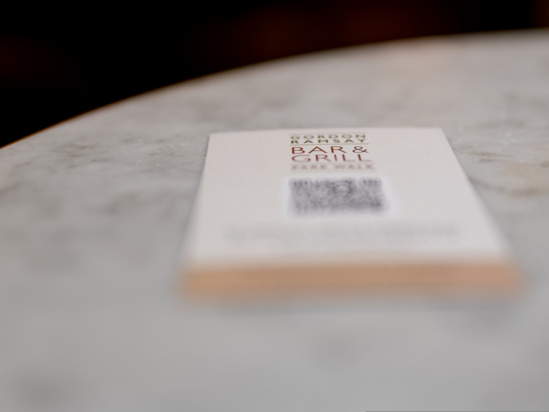 Business card on a marble table with Gordon Ramsay Bar & Grill logo and a QR code on the back, out of focus.