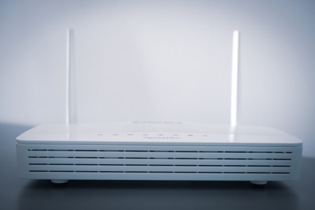 White wireless router with two vertical antennas on a dark tabletop, front vents visible.