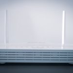 White wireless router with two vertical antennas on a dark tabletop, front vents visible.