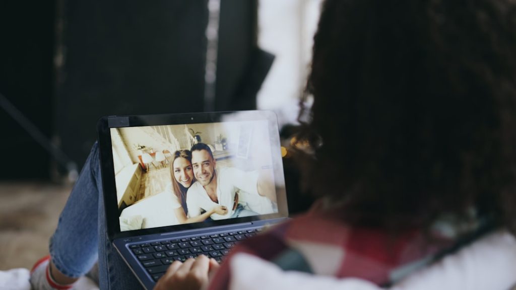 Person watching a video call: laptop screen shows a smiling couple taking a selfie while chatting online.