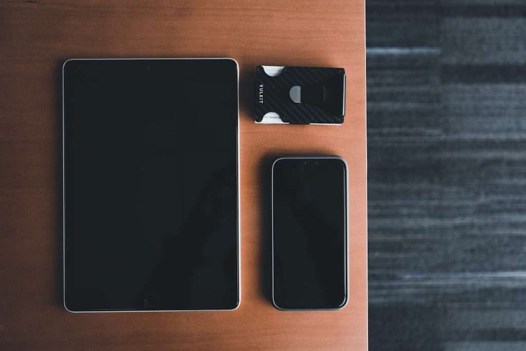 Tablet and smartphone with a small black accessory labeled 'VUKIT' on a wooden desk surface.