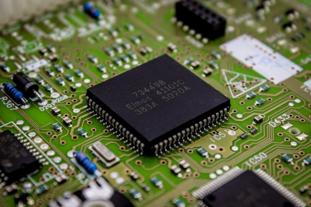 Close-up of a black integrated circuit on a green printed circuit board with surrounding resistors and connectors.