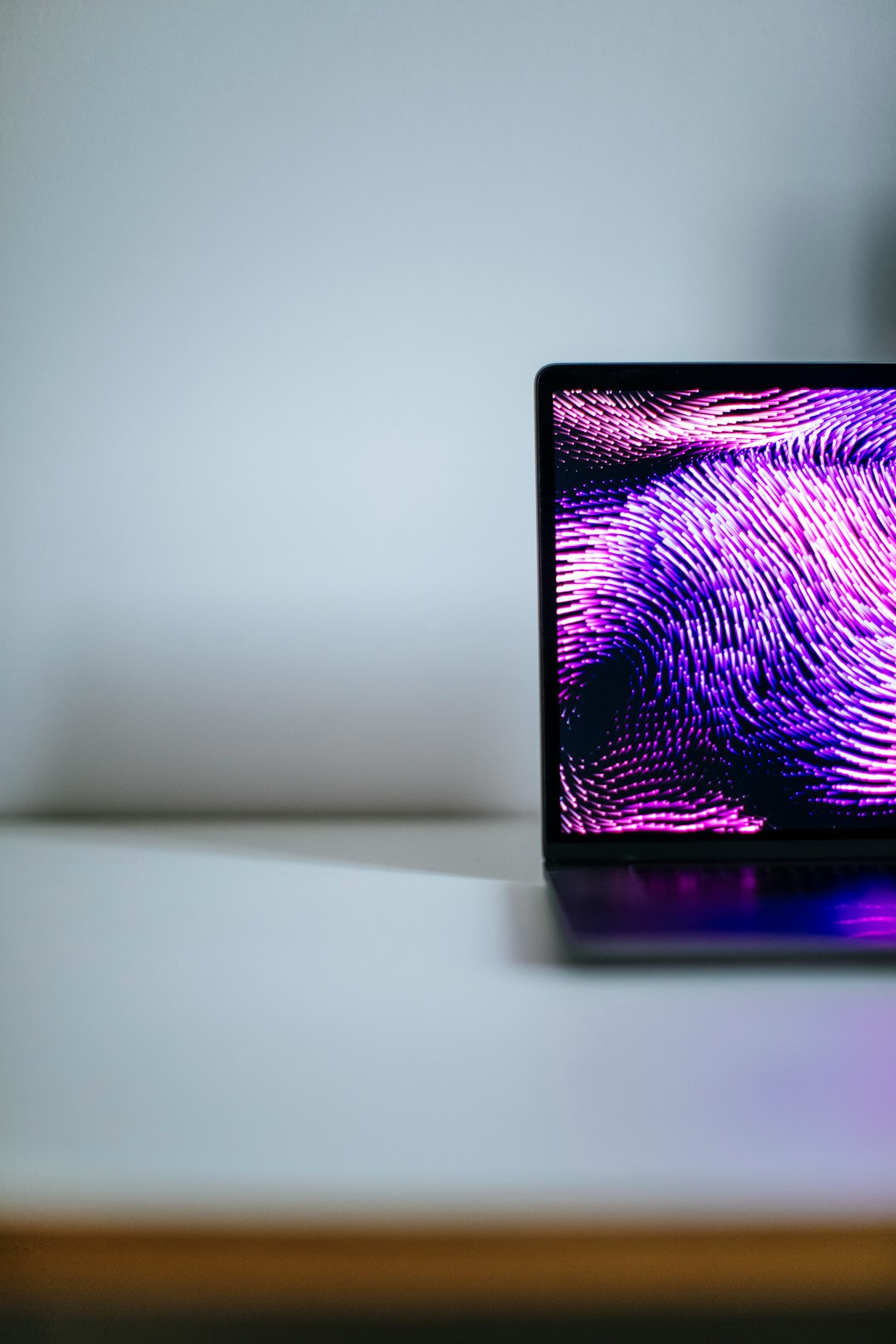 Partial view of a laptop on a white desk with a vibrant purple-pink abstract wallpaper on the screen.