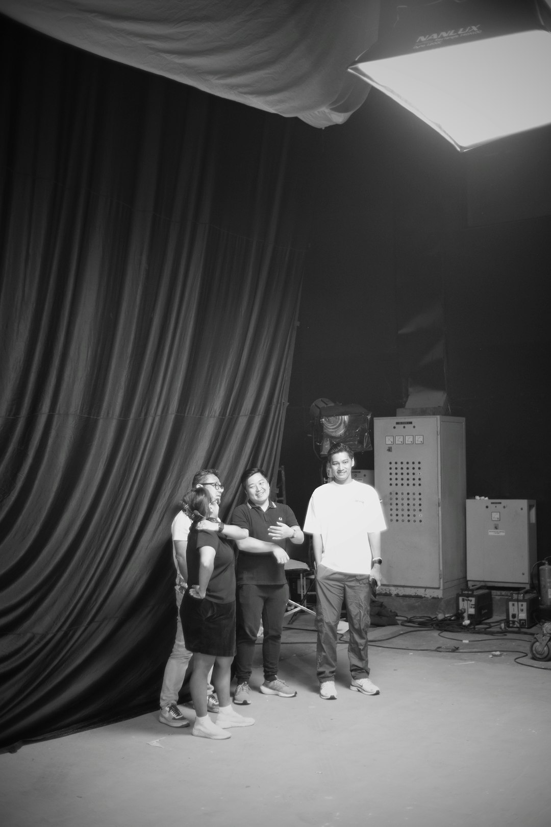 Five people posing together in a studio beside curtain backdrop and stage equipment, smiling at the camera.