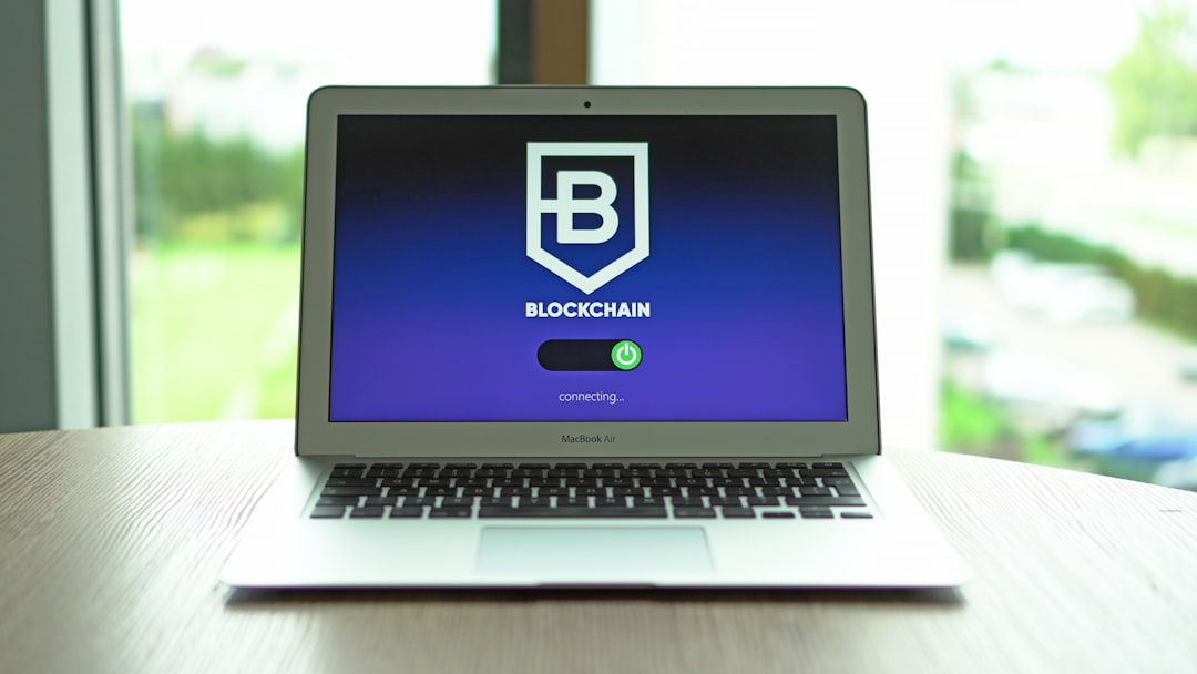 MacBook Air on a wooden table displaying a Blockchain logo with a 'connecting...' progress bar on the screen.