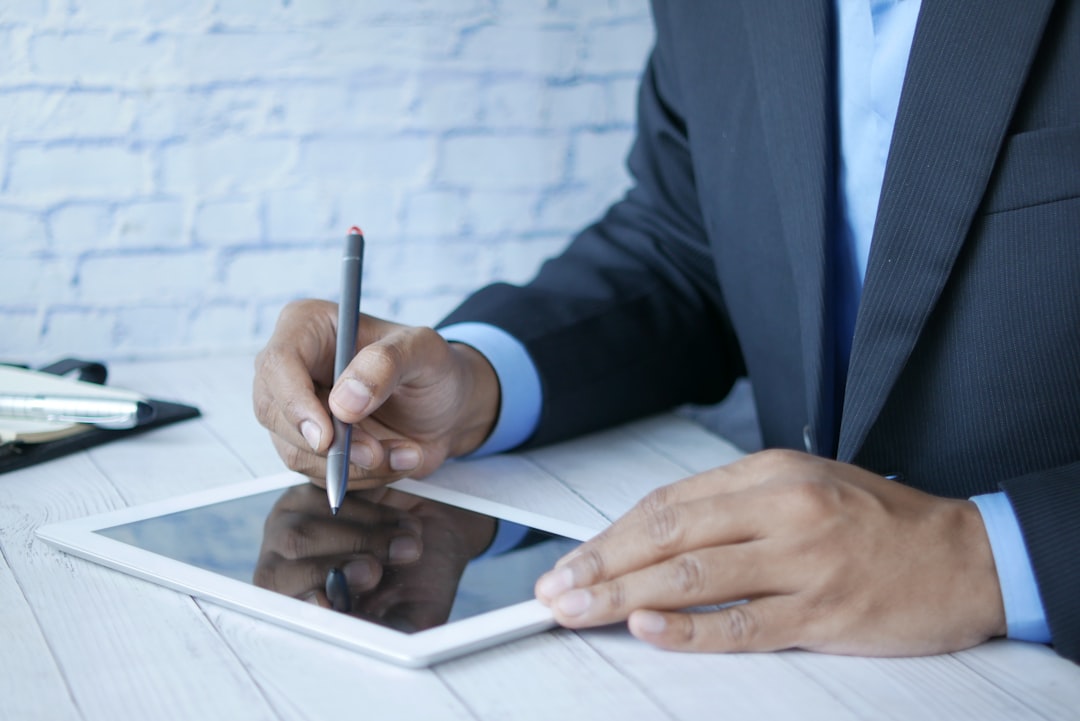 Person in a dark suit uses a stylus on a tablet at a light desk.