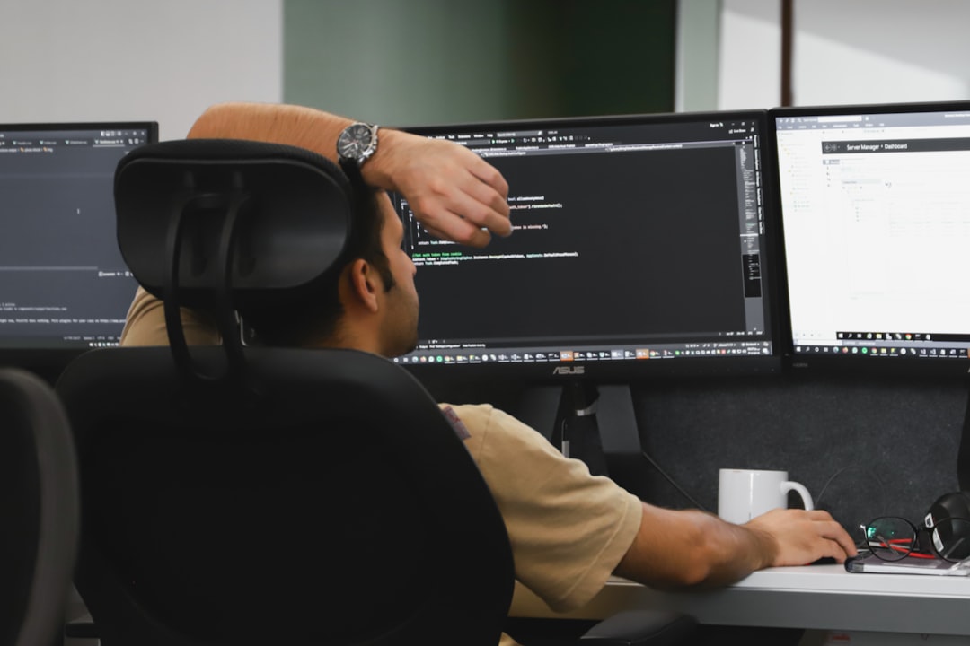 Person seated at a desk coding on a triple-monitor setup, with code on the center screen and a dashboard on the right.