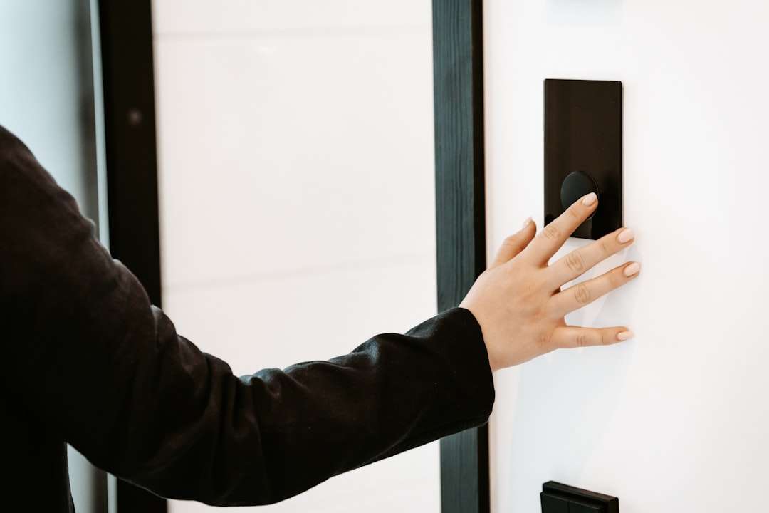 Person pressing a black rectangular wall switch on a white wall.