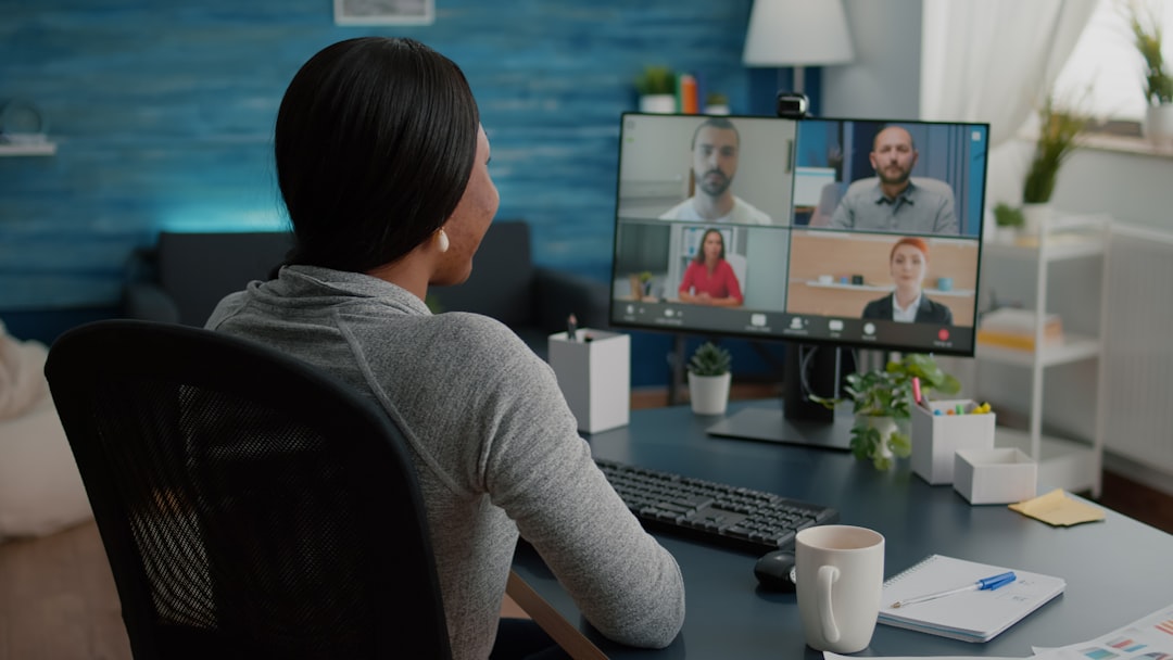Person sitting at a desk participating in a video conference, monitor displaying a grid of six attendees.