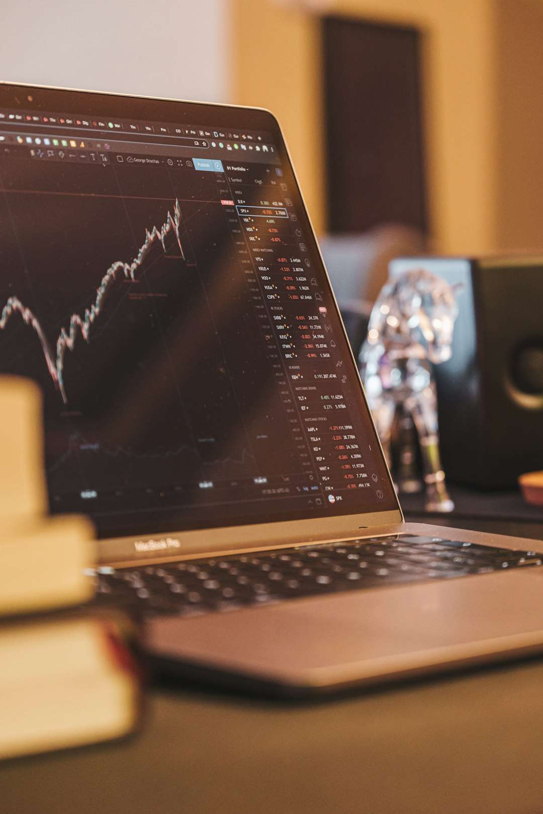 Laptop open to a trading dashboard showing a rising stock chart and market tickers on screen.
