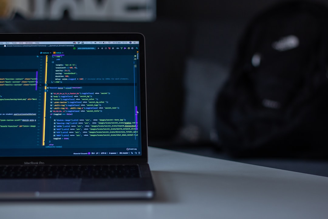Laptop with a code editor displaying colorful syntax on the screen, on a white desk, blurred backpack in the background.