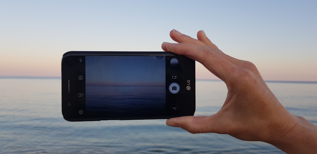Hand holding a smartphone horizontally to photograph a sunset over calm ocean.