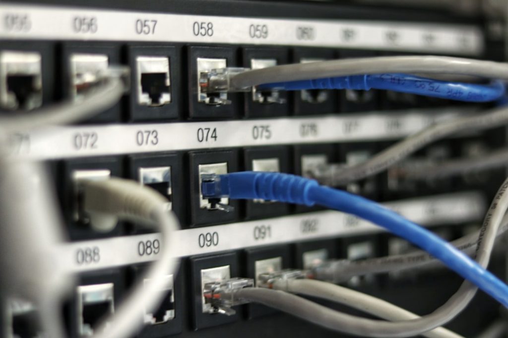 Rack-mounted network switch with blue and gray Ethernet cables plugged into numbered ports and labels visible on the panel.