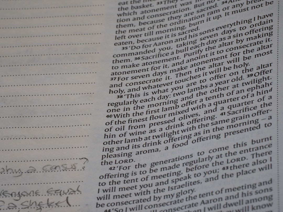 Close-up of a Bible page with densely printed verses on the right; a lined notebook with handwritten notes is on the left.