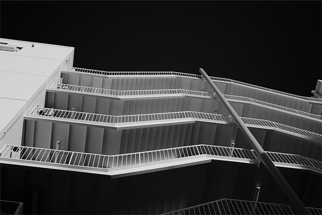 Black-and-white exterior stairwell of a modern building, with zigzag metal fire escapes along multiple levels.