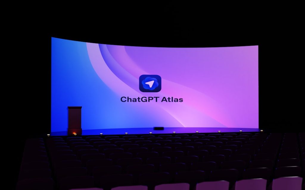 Empty auditorium facing a curved projection screen showing the ChatGPT Atlas logo on a purple-blue gradient backdrop and dark seating.